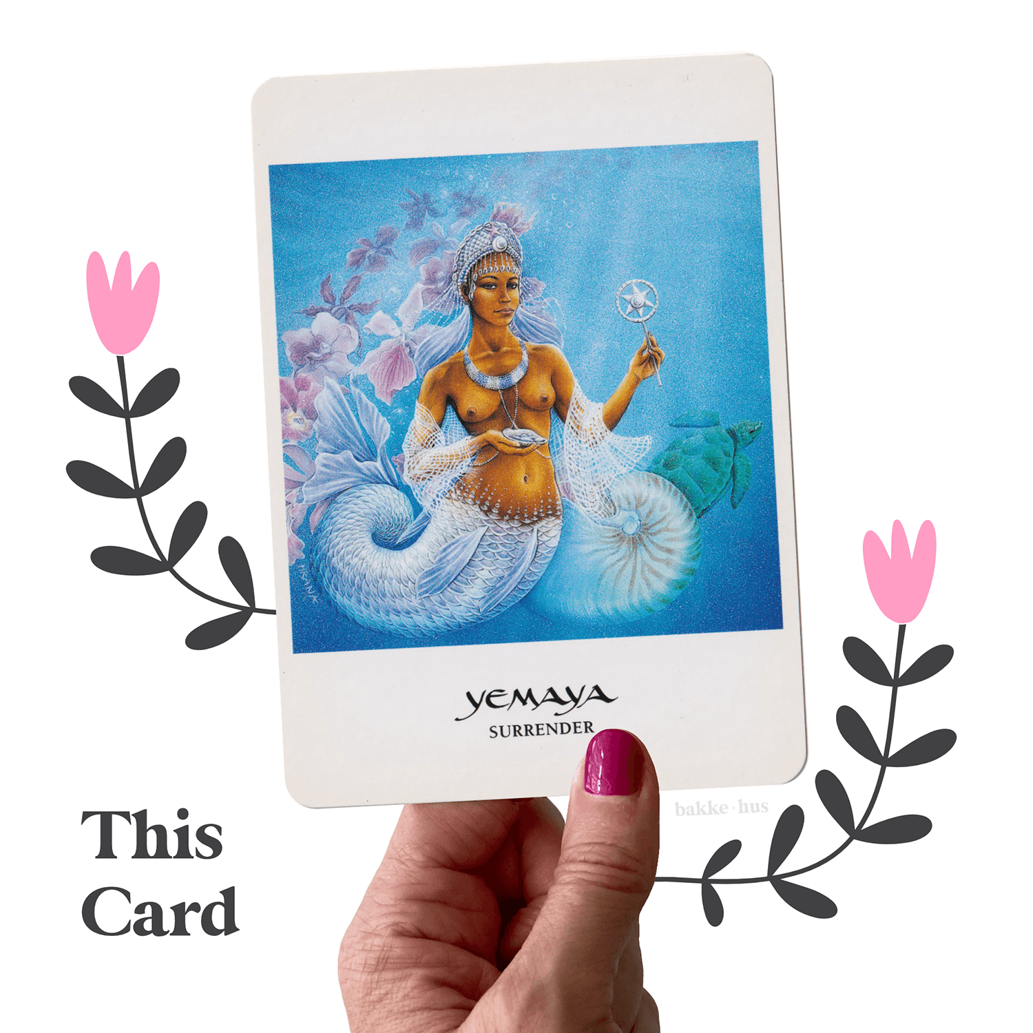 A female hand holding the Yemaya Oracle Cards from The Goddess Oracle deck by Amy Sophia Marashinsky. The image also contains two pink & black illustrated flowers and the words 'This Card" and bakkehus logo.